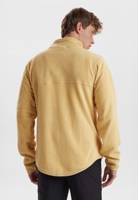 Geel fleece sweatshirt met lange mouwen, een hoge kraag, een gebogen zoom en een gestructureerd oppervlak, met contrasterende naden langs de achterkant.