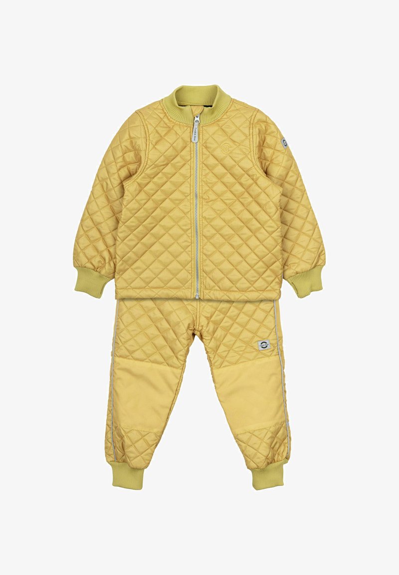 Tuta giallo trapuntato con giacca con zip e polsini elastici. I pantaloni presentano un colore uniforme e una piccola toppa di lato.