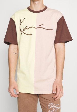 Camiseta de mangas cortas con bloques de color en tonos amarillo pálido, rosa claro y marrón. Material de algodón suave con logo bordado en el pecho.