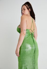 Vestido maxi de satén verde con una silueta elegante, tirantes finos, diseño de espalda descubierta y detalles de lazo ajustables.