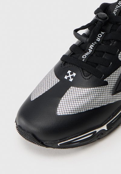 Μαύρο αθλητικό παπούτσι με επάνω μέρος από ύφασμα διχτυού, λευκές λεπτομέρειες και υφασμένο από καουτσούκ πέλμα. Διαθέτει κορδόνια και λογότυπο στη πλευρά.