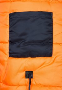 Orange puffer jacket fabric with a square black patch pocket. Features a drawstring at the hem, made from a smooth, lightweight material.