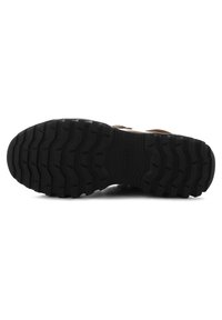 Black rubber sole with deep tread pattern, featuring raised grooves for traction. Smooth upper material with a natural tan leather accent.