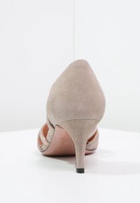 Beige suede high-heeled shoe with a pointed toe, cut-out sides, and a slender heel. Smooth texture and minimalistic design.