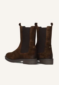Een paar donkerbruine suède Chelsea-boots met zwarte elastische zijpanelen en lage gestapelde hielen, gefotografeerd van de achterkant en zijkant.