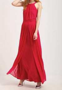 Maxiklänning i klar rosa, tillverkad av lättviktigt tyg. Har en plisserad bodice och flödande kjol. Utsmyckad med en halterneck.