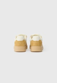 Brune og kremfarvede sneakers lavet af ruskind og læder. Har en polstret krave og en gummisål med mærkenavnet "ARKK" præget.