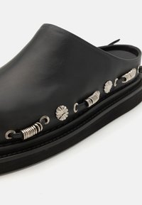 Fekete bőr slip-on cipő kerek orral, ezüst dekoratív részletekkel az oldalon és texturált talppal.
