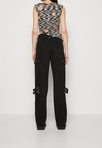 Pantalones cargo anchos y negros con múltiples bolsillos y detalles metálicos. La parte superior presenta un diseño de punto texturizado sin mangas con recortes.