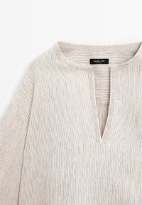 Haut beige à rayures verticales, en tissu léger, design en V, avec un plastron subtil et des manches trois-quarts. Étiquette de marque visible.