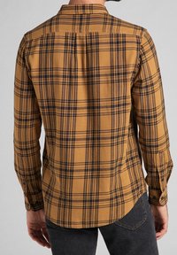 Camicia a quadri di colore giallo senape con linee nere e marroni, dotata di maniche lunghe, colletto con bottoni e orlo curvo.