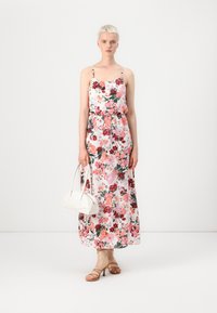 Floral maxi dress with thin straps, featuring pink, red, and green patterns on a white background. Paired with a white handbag and strappy sandals.
