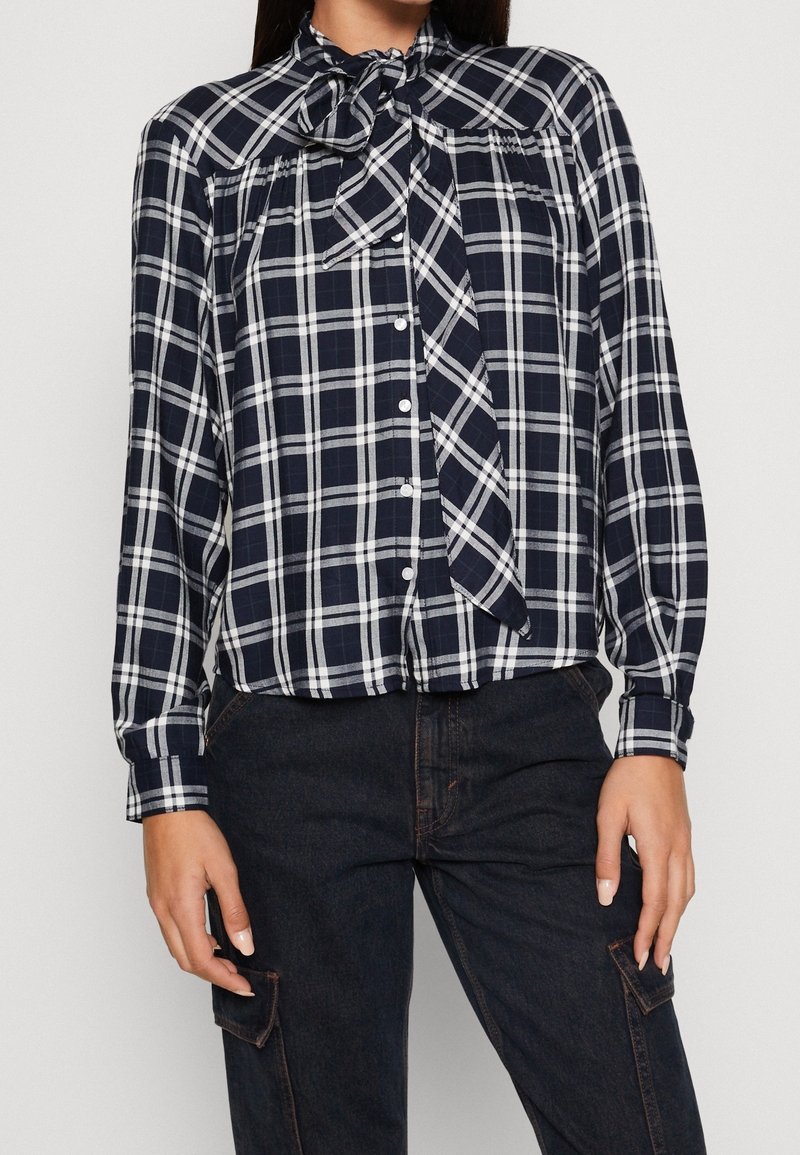 Navy and white plaid button-up shirt with long sleeves and a bow tie collar. Soft fabric, loose fit, and front button closure.