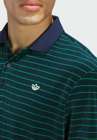Polo-shirt rayé bleu marine avec des rayures horizontales vertes, doté d'un col et de trois boutons, orné d'un logo blanc brodé.