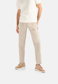 Pantaloni beige su misura con una texture liscia, indossati con una t-shirt di colore chiaro e scarpe beige con suole e lacci crema.