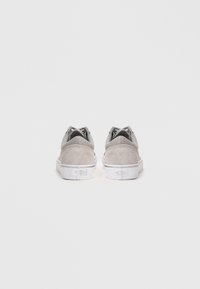 Grey suede sneakers with a low-top design, white rubber soles, and contrasting textile accents on the upper, featuring logo details on the heel.
