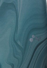 Texturovaná tkanina v odstínu modrozelené s vlnitými vzory. Obsahuje vystouplé kruhové akcenty v různých velikostech, což zvyšuje hloubku a vizuální zajímavost.