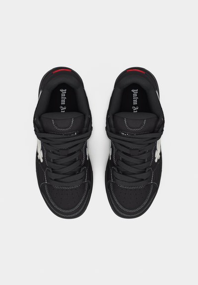 Ζευγάρι μαύρα αθλητικά παπούτσια χαμηλού ύψους με λευκά ανθισμένα σχέδια στα πλαινά και μαύρα κορδόνια, σε εικόνα από ψηλά πάνω σε ανοιχτό φόντο.