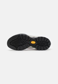Vibram yttersåle på en sko med et teksturert svart gummimønster og en synlig gul logo. Overmaterialet er lys grått med subtile designlinjer.