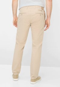 Beige katoenen broek met rechte pasvorm, voorzien van twee achterzakken en een gladde textuur. Draagt beige en witte sneakers.