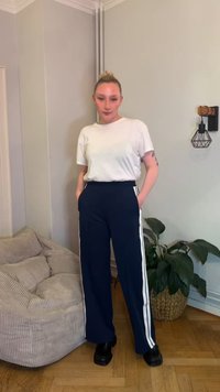 Marineblauwe broek met hoge taille en witte zijstrepen, gecombineerd met een aansluitend wit T-shirt. Glad stof, losse pasvorm en platte schoenen.