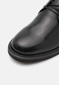 Black leather shoe featuring a smooth finish, rounded toe, and contrasting rubber sole with visible stitching detail.