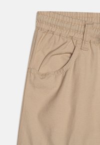 Beige broek met gestructureerde stof, voorzien van een elastische tailleband, een gebogen zak en contrasterende stiksels.