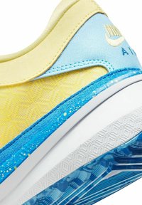 Sneaker giallo e azzurro chiaro con tessuto testurizzato, dettagli lisci, suola intermedia bianca e suola in gomma con motivo e dettagli blu e gialli.