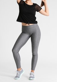 Svart kort topp med meshärmar, knuten i midjan, tillsammans med figurnära grå leggings och grå sportskor med mintgröna detaljer.