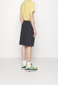 Dark gray shorts with a relaxed fit, featuring back pockets. Paired with a yellow t-shirt and multicolored athletic sneakers.