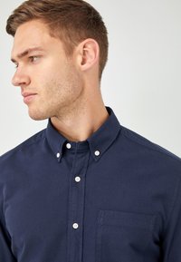 Marineblauwe button-up shirt van katoen, met een klassieke kraag, een borstzak en witte knopen langs de sluiting. Soepele textuur.