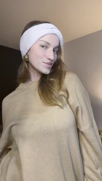 Pull en maille beige à manches longues, associé à un serre-tête blanc torsadé. De grandes boucles d'oreilles dorées viennent compléter le look.