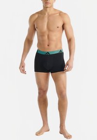 Černé boxerky s tyrkysovým elastickým pasem s jemným vzorem loga. Materiál působí hladce a pružně.