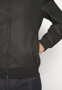 Giacca bomber nera trapuntata con chiusura a zip, polsini a coste e due tasche laterali, realizzata in tessuto testurizzato.