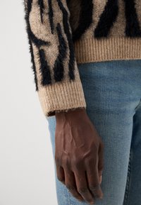 Stickad tröja med en texturerad beige kropp och svarta pälsliknande ränder. Ärmslutet är ribbat och armen är kombinerad med blå denimjeans.