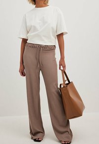 Weißes Baumwoll-T-Shirt in lockerer Passform, kombiniert mit hellbraunen, gerippten, weit geschnittenen Hosen mit elastischem Bund und Kordelzug. Braune Tragetasche.