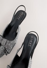 Čierne lodičky s mašľou ozdobenou kryštálikmi, otvoreným zadným dielom a nastaviteľným remienkom, s textúrovaným vrškom a hladkou podšívkou.