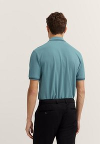 Polo turchese con colletto classico e maniche corte, con accenti a strisce scure. Pantaloni neri con tasche posteriori.