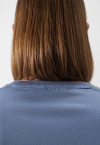 T-shirt in cotone di un blu tenue, con scollatura a girocollo e cuciture visibili lungo il colletto. Texture liscia con una vestibilità rilassata.