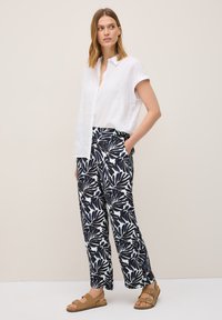 White linen short-sleeve shirt paired with navy-blue leaf-patterned trousers and brown sandals. Trousers have side pockets and a relaxed fit.