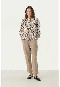 Peplum top in cream with black and brown floral pattern; long sleeves with elastic cuffs. Loose beige linen trousers; black slip-on shoes.