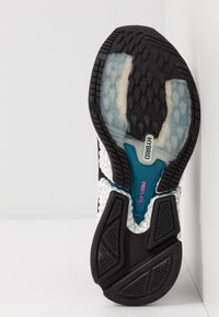 Semelle d'une chaussure de course hybride noire et blanche avec grip texturé et étiquettes roses "PROPLATE" et noires "HYBRID" bien visibles.
