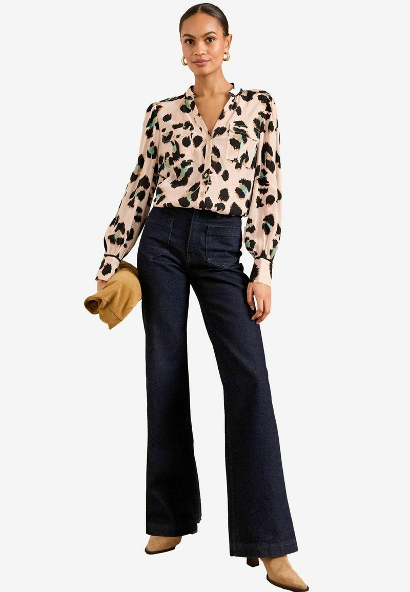 Svijetloružičasta bluzica s crnim i tirkiznim printom na leopard pjege, s prednjim dugmadi, u kombinaciji s tamnoplavim farmerkama visokog struka u širokom kroju i bež gležnjačama.
