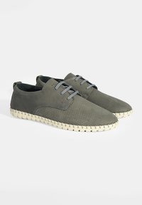 Chaussures en cuir perforé grises avec bout arrondi, lacets gris et semelle tissée beige. Le design présente une texture lisse et des accents minimalistes.