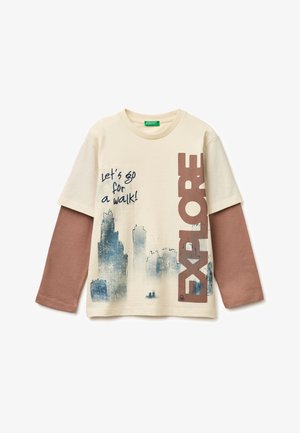 Cremefarbenes, langärmeliges, geschichtetes T-Shirt mit braunen Ärmeln, Stadtsilhouetten-Print, Text "Lass uns spazieren gehen!" und großem, vertikalem Aufdruck "ENTDECKEN".