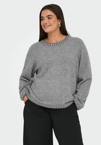 Grijze gebreide trui met een ronde hals, geribde manchetten en zoom. Gecombineerd met zwarte wijde broek, die een ontspannen pasvorm laat zien.