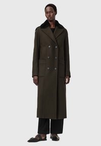 Um longo casaco verde oliva com um design de doble peito, grandes bolsos e um colarinho de pele sintética preta. Textura suave, silhueta ajustada.