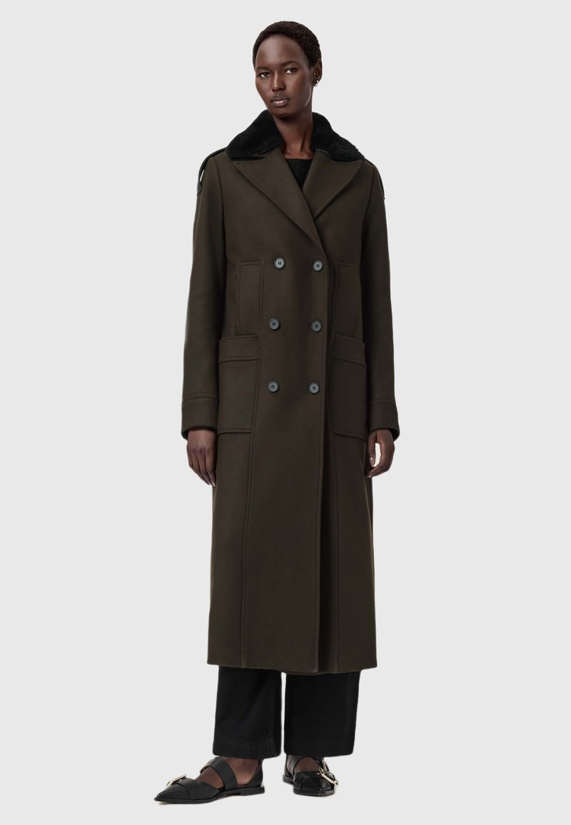 Um longo casaco verde oliva com um design de doble peito, grandes bolsos e um colarinho de pele sintética preta. Textura suave, silhueta ajustada.