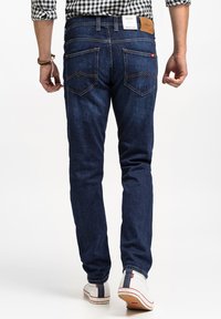 Ciemnoniebieskie dżinsy o dopasowanym kroju, z tylnymi kieszeniami ozdobionymi wzorem w zygzak oraz skórzaną łatą na pasku.