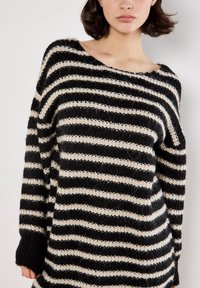 Sort og creme stribet striktrøje med løs pasform, bred halsudskæring og lange ærmer. Stoffet har et struktureret, blødt udseende.